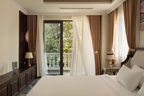 Camera d'albergo con un letto grande, un comodino, una lampada e vista su un balcone con tende.