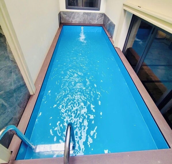Una piscina rettangolare con superficie d'acqua cristallina e blu, circondata da un pontile in legno e un muro rivestito di piastrelle.