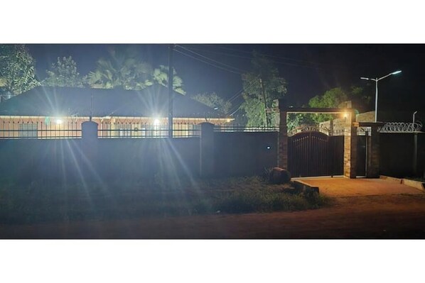 A gated property at night with a well-lit entrance and a metal fence.