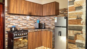 A kitchen with wooden cabinets, a stove, a microwave, and a refrigerator. - Alfred Villas Gulu Five Bed Room Furnished House (Gulu City)
