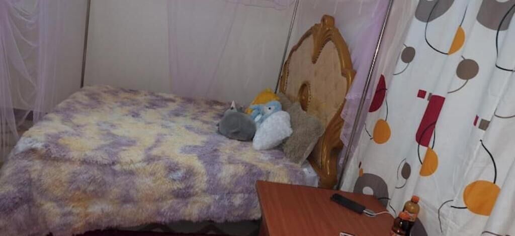 Ein Bett mit einem gemusterten Überwurf, einem Holzkopfstück und einem Nachttisch mit einer Flasche und einer Fernbedienung.