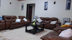A living room with brown leather sofas, a black coffee table, and a white carpet. - Alfred Villas Gulu Five Bed Room Furnished House (Gulu City)