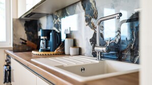 Une cuisine avec un évier blanc, une machine à café et un dosseret en marbre.