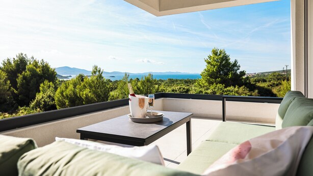 Un balcon avec une table, une bouteille de champagne et des verres, donnant sur un paysage magnifique, avec des arbres et des montagnes.