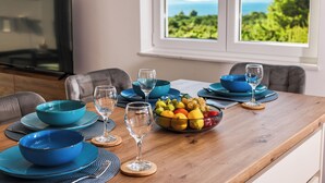 Une table à manger dressée avec des bols, des assiettes et des verres à vin bleus, et un panier de fruits placé au centre.