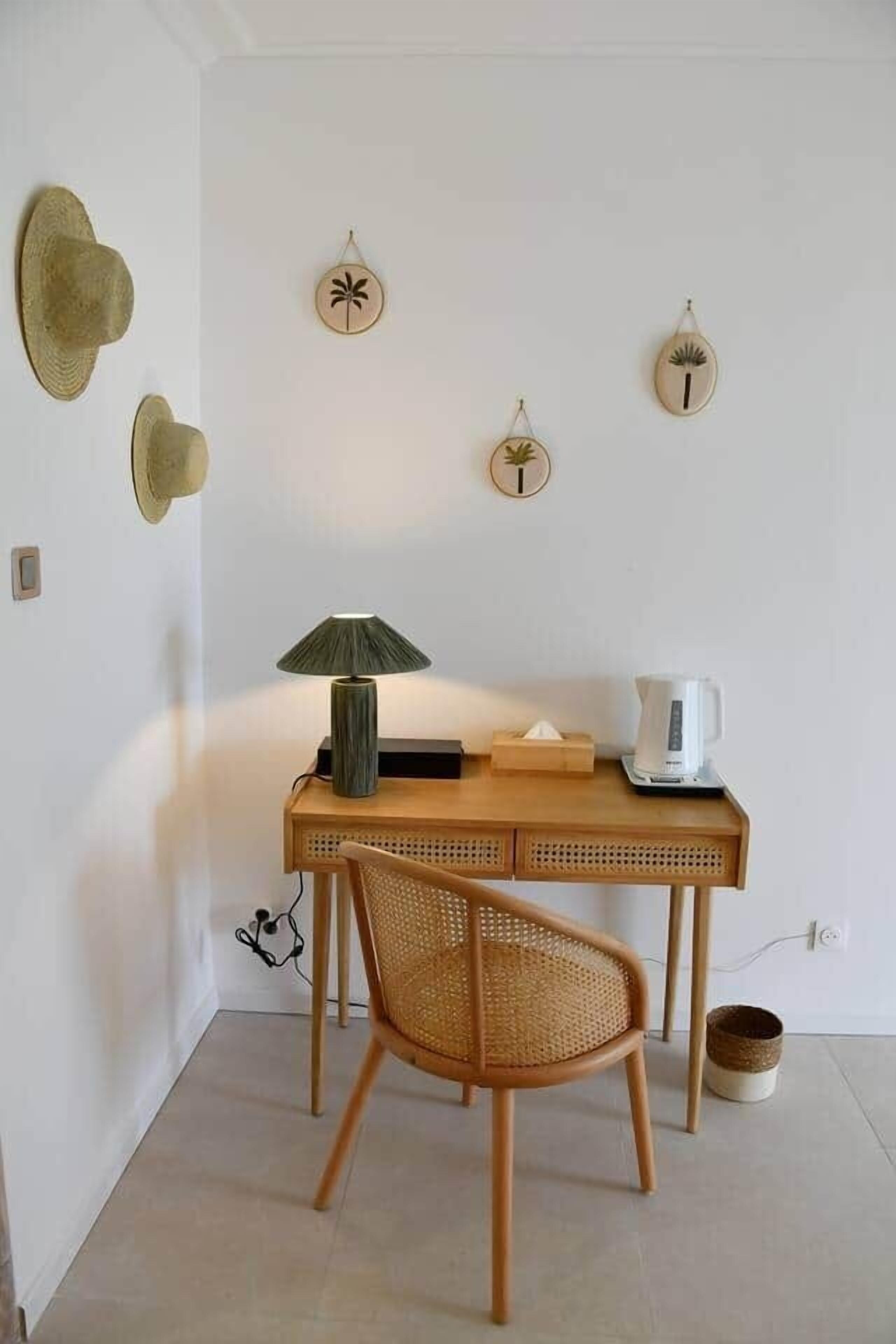 A room with a wooden desk, a wicker chair, a lamp, and wall decorations including hats and palm tree signs.