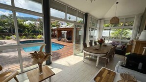 A spacious living area with large windows, a pool, and a dining set. - Villa Kokoro - Monstera room (Saint-Paul)