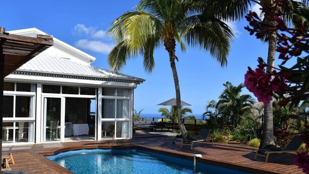 A poolside area with a wooden deck, lounge chairs, and a view of the ocean. - Villa Kokoro - Monstera room (Saint-Paul)