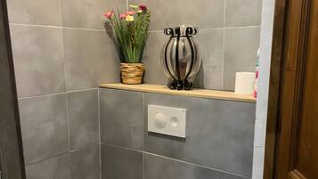 Een badkamer met een toilet, een plankje met een vaas en bloemen, en een toiletrolhouder.