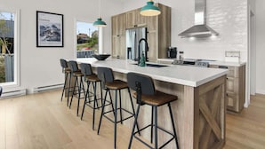 A modern kitchen with a large island, bar stools, pendant lights, and a view of the outside.