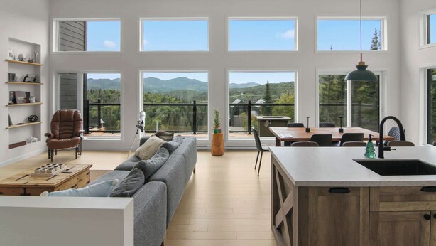 A spacious living area with a sofa, a dining table, and a kitchen area with a large window offering a mountain view.