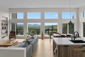 Un vaste espace de vie comprenant un canapé, une table à manger et un coin cuisine avec une grande fenêtre donnant sur les montagnes.