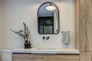 A bathroom with a white countertop, a mirror, a towel rack, and a wooden cabinet. - Remontée | Tavata Chalets | Valinouët (Saint-David-de-Falardeau)