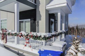 A two-story house with a covered porch, a garage, and a snow-covered driveway. - Remontée | Tavata Chalets | Valinouët (Saint-David-de-Falardeau)