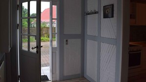 A room with a door leading to a garden, a kitchen area with a stove, and a white brick wall with decorative panels.