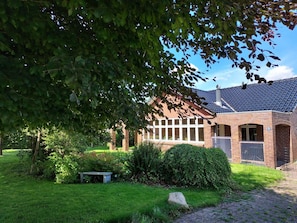 A brick building with a tiled roof, surrounded by a well-maintained garden with a bench and a large rock. - 4 Star Holiday Home in Tonder (Tonder)