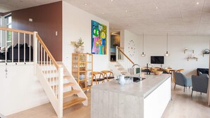 A modern interior with a central island, wooden staircase, and a dining area. - 5 Star Holiday Home in Sjolund (Sjølund)