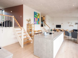 Ein modernes Interieur mit einer zentralen Kücheninsel, einer Holztreppe und einem Essbereich.