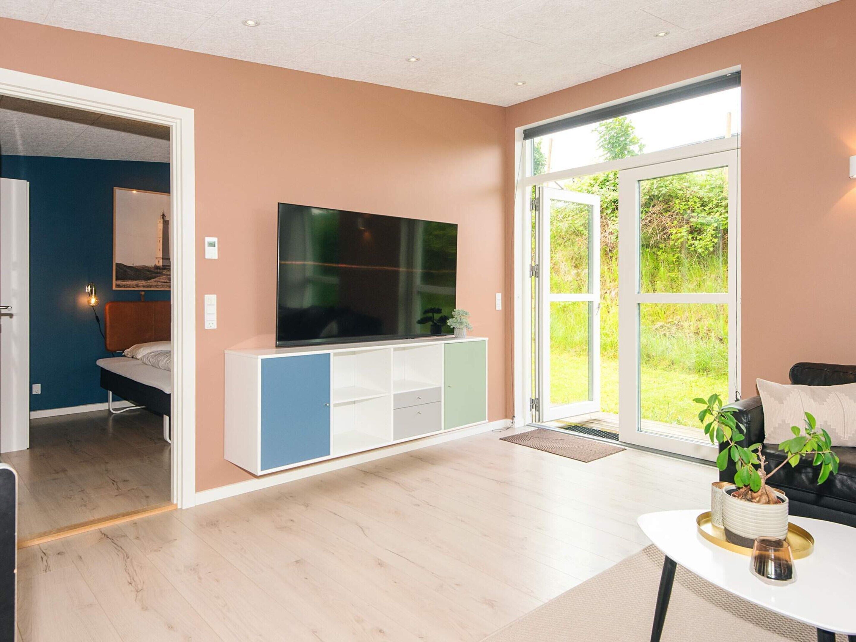 A modern living room with a flat-screen TV, a sofa, a coffee table, and a sliding glass door leading to a garden.