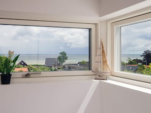A room with a large window overlooking a body of water, a potted plant, and a small sailboat model. - 5 Star Holiday Home in Sjolund (Sjølund)