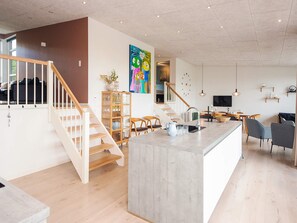Ein modernes Interieur mit einer zentralen Kochinsel, einer Holztreppe und einem Essbereich.