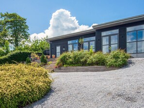 Un bâtiment moderne à la façade sombre, doté de grandes fenêtres et d’une allée gravillonnée.