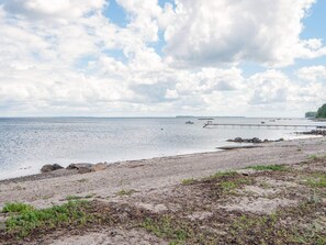 Une plage côtière avec une jetée qui s’avance dans l’eau, un rivage rocheux et un ciel dégagé.