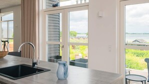 A kitchen with a sink, a blue pitcher, and large windows with views of greenery and a body of water. - 5 Star Holiday Home in Sjolund (Sjølund)