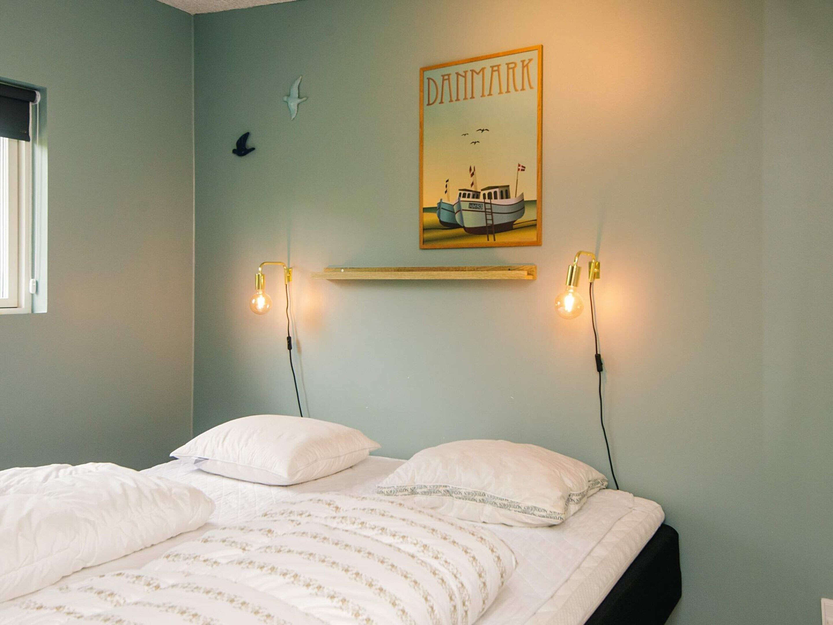 Ein Schlafzimmer mit einem Bett, zwei Wandleuchten, einem gerahmten Bild eines Bootes und einer kleinen Vogeldekoration.