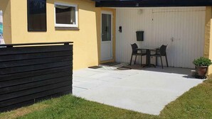 A single-story building with a yellow exterior and a white garage door. There is a black bench in front of the building, and a small table with two chairs is positioned near the garage door. - 5 Star Holiday Home in Lokken (Lokken)