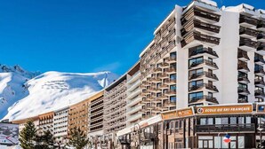 A multi-story hotel with balconies, a ski resort sign, and snow-covered mountains in the background. - Large Studio 4 - Comfortable - Balcony - Lake View (Tignes)