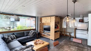 Een moderne woonkamer met een bank, televisie, houten entertainmentmeubel, eettafel en keukenhoek.