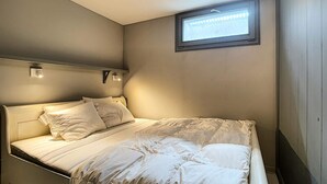 Een eenpersoonskamer met een hoofdeinde, twee bedlampen en een raam met zonwering.