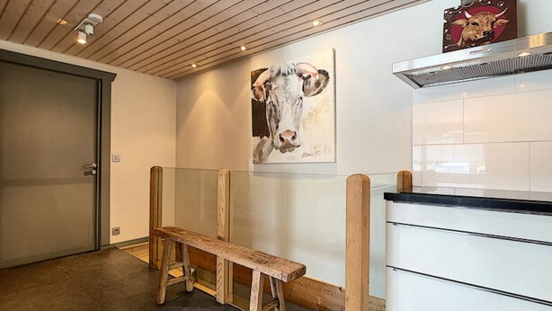 Een gang met een houten bankje, een witte betegelde muur en een schilderij van een koe.
