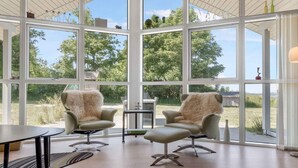 Una habitación amplia con ventanas grandes, dos sillones, una mesita y una alfombra.