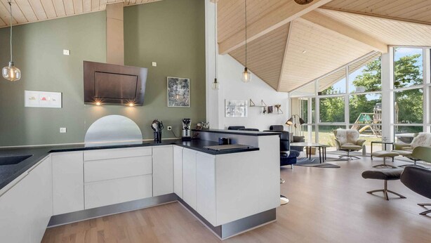 Una cocina moderna con una isla central, techo de madera y ventanas amplias que ofrecen vistas al exterior.