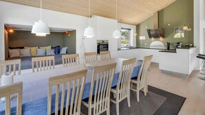 Una cocina moderna con horno empotrado, un comedor con sillas de madera y mantel azul, y una zona de estar acogedora con una cama y almohadas.