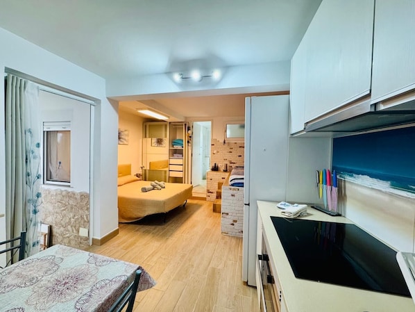 A compact room with a bed, a small table, a kitchenette, and a bathroom.