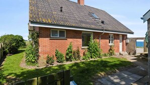 A single-story brick house with a sloped roof, a small front porch, and a garden with various plants. - 5 Star Holiday Home in Grenaa (Grenaa)