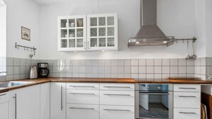 A kitchen with white cabinets, a stainless steel range hood, and a tiled backsplash. - 5 Star Holiday Home in Grenaa (Grenaa)