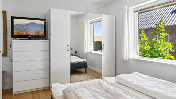 A bedroom with a bed, a TV on a cabinet, a window with a view of greenery, and a mirror reflecting the room. - 5 Star Holiday Home in Grenaa (Grenaa)