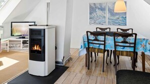 A cozy room with a modern fireplace, a dining table with chairs, and a large window with a view of the sea. - 5 Star Holiday Home in Grenaa (Grenaa)