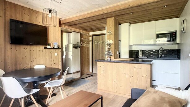 A modern kitchen with a microwave, stove, and wooden cabinetry. There is a dining area with a round table and chairs. - Renovated Apartment Near the Slopes (Courchevel)