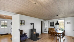 Un'ampia stanza con pavimento in legno, zona pranzo con sedie di legno, stufa a legna integrata e una grande finestra che offre luce naturale.