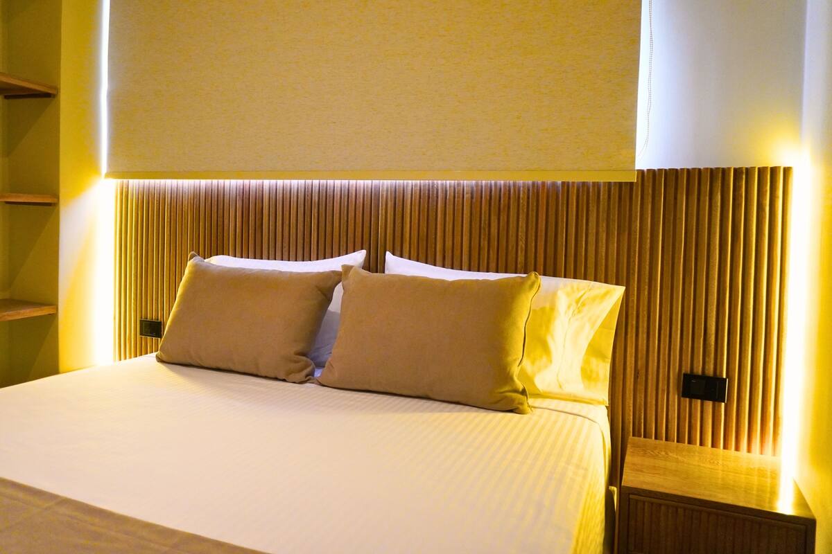 Une chambre d’hôtel avec un lit, deux oreillers, une table de chevet et une étagère fixée au mur.