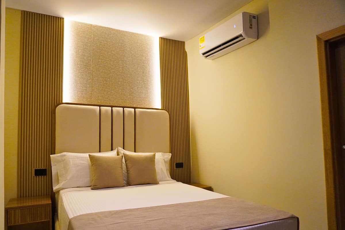 Une chambre d’hôtel équipée d’un lit, d’un climatiseur fixé au mur et d’une fenêtre avec des stores verticaux.