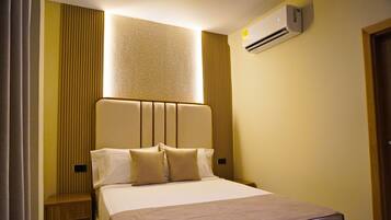 Quarto de hotel com uma cama, ar condicionado fixado na parede e janela com persianas verticais.