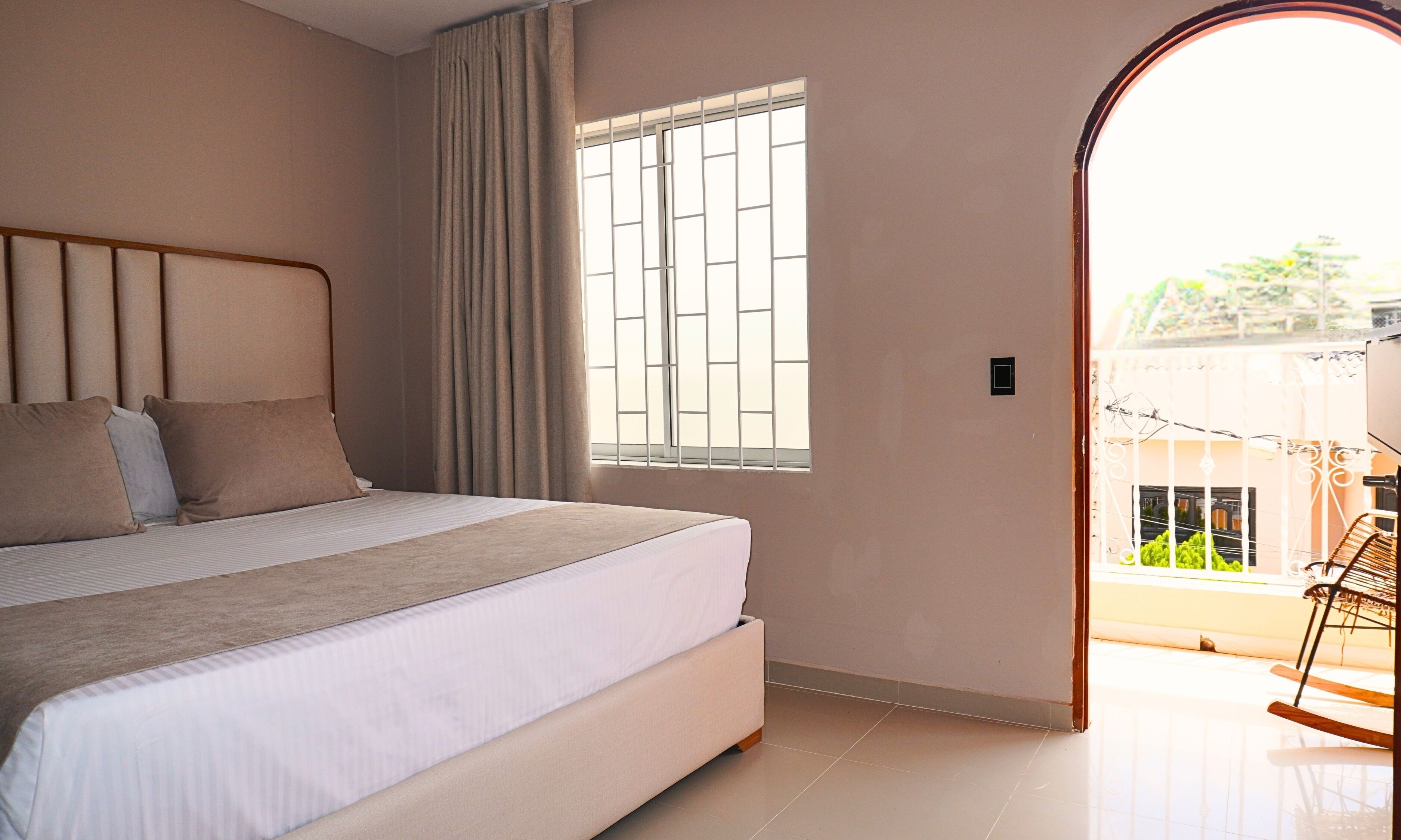 A bedroom with a bed, curtains, a window with bars, and a view of the outside.