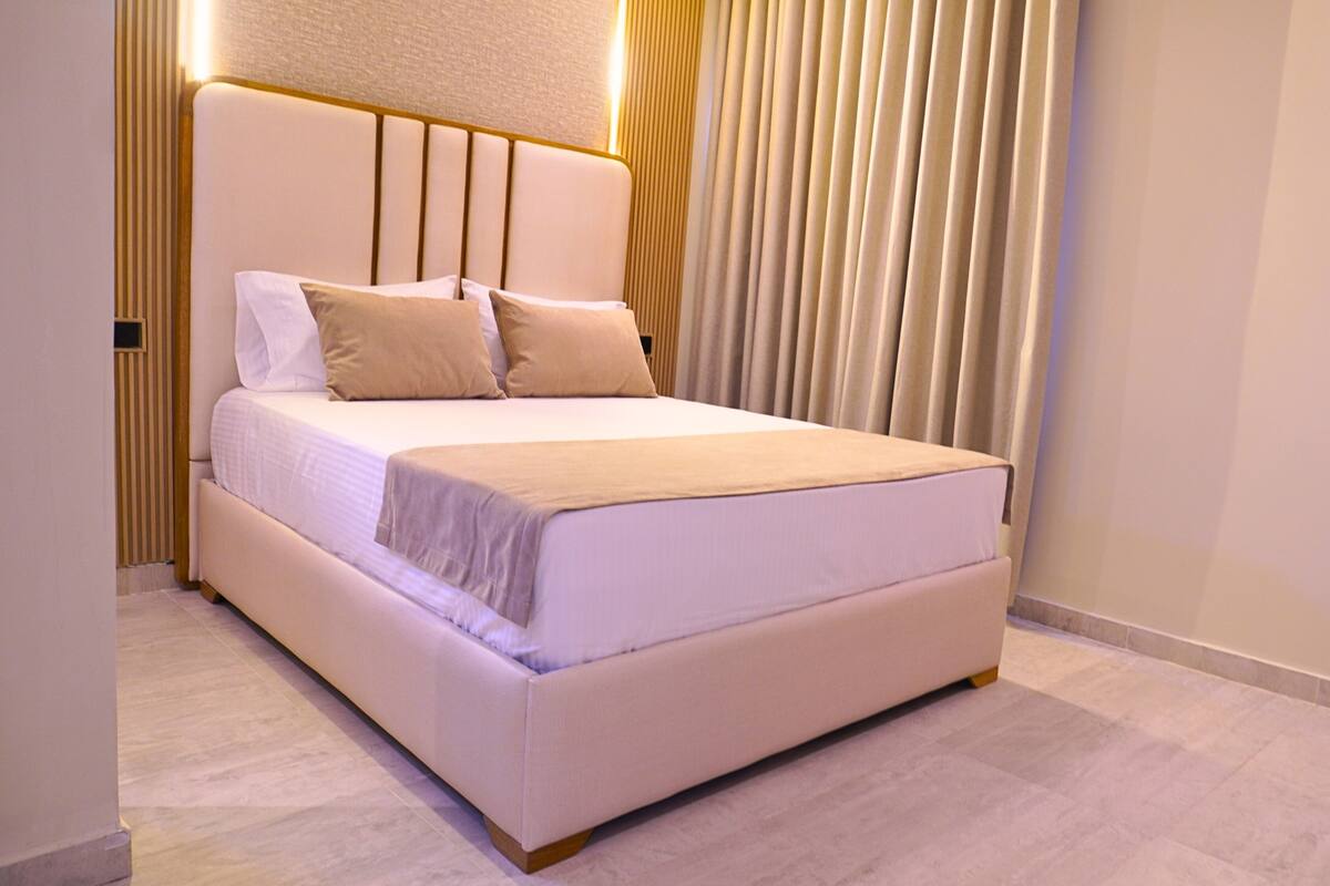 Une chambre à coucher moderne avec un grand lit, une tête de lit ornée de lignes verticales et un rideau à la fenêtre.