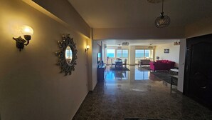 Un hall d’hôtel doté d’un sol en marbre poli, d’un grand miroir encadré d’un motif en forme de soleil et d’un espace détente avec un canapé rouge et une table à manger.